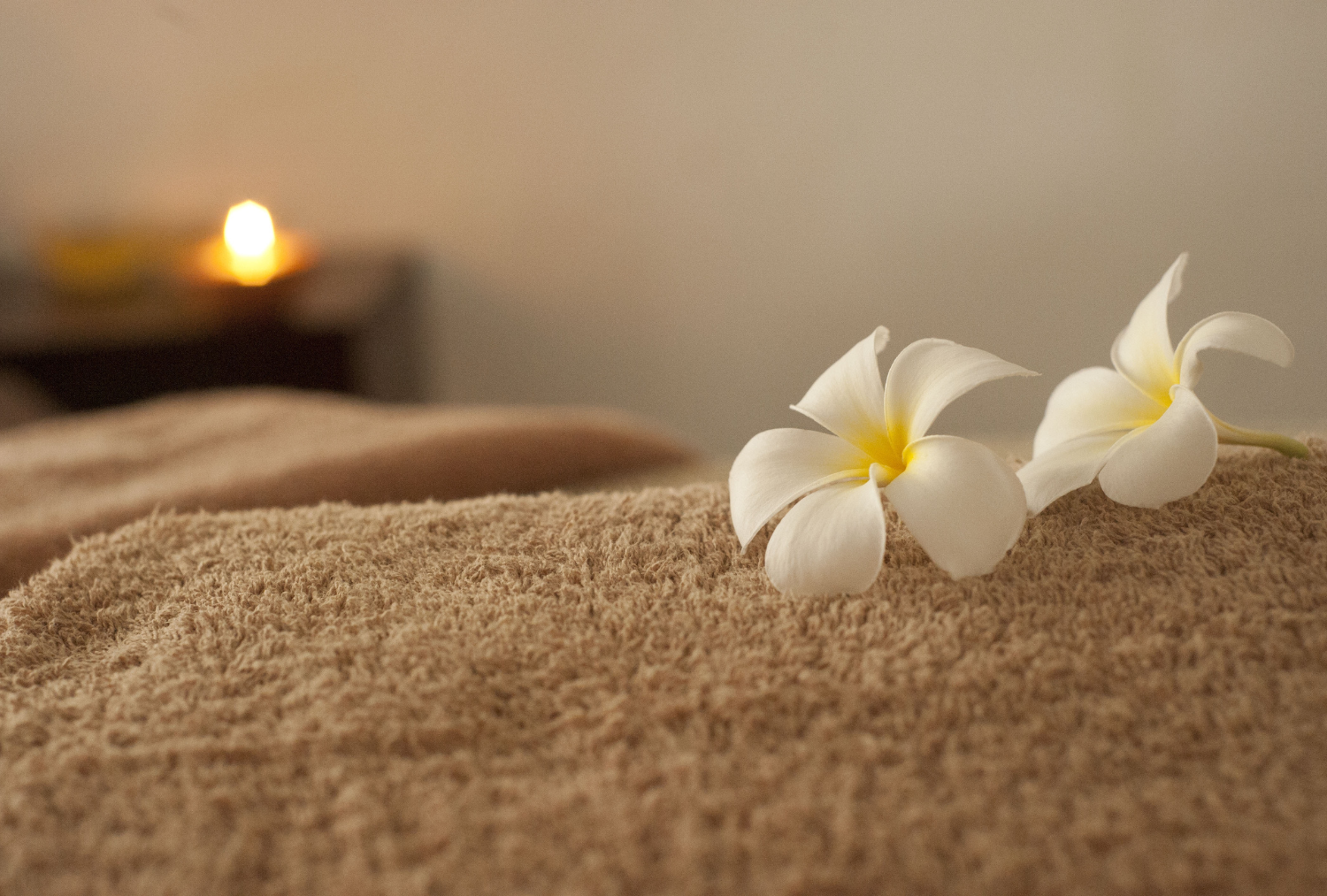 White and yellow flowers on a brown towel with a lit candle in the background at the Wentworth.