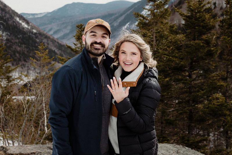 A newly engaged couple poses for a photo on a mountain in Jackson, NH