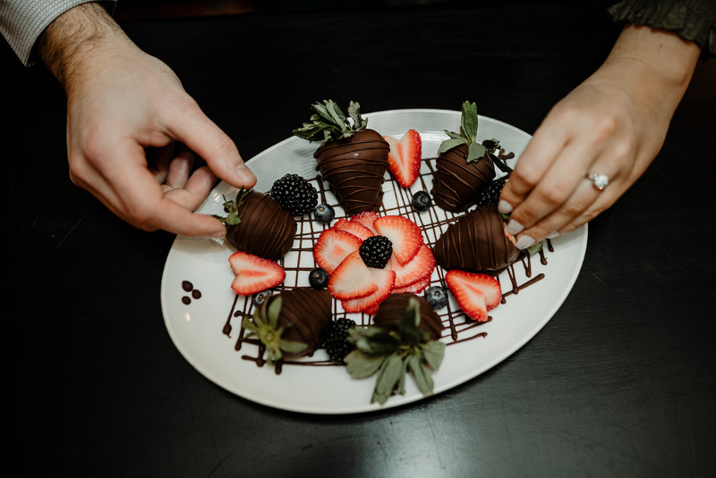 two hands placing strawberries on a plate of chocolate covered strawberries with blackberries at the Wentworth inn.