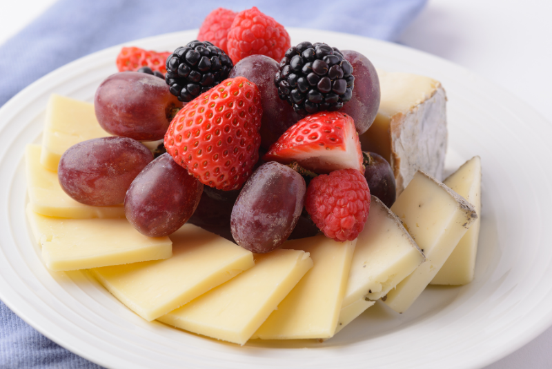 A plate of strawberries, grapes, raspberries berries , and blackberries with cheese.