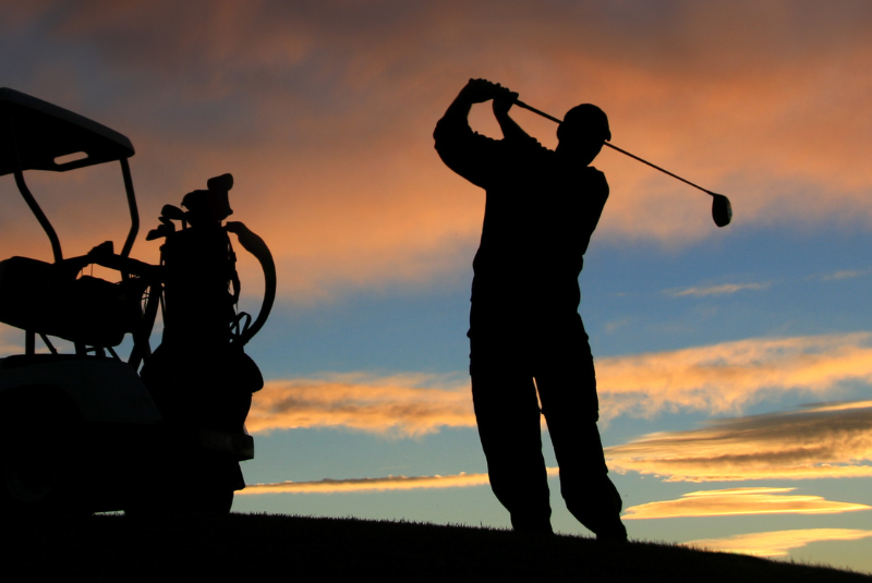 A silhouette of a man in the sunset swinging a golf club near the Wentworth