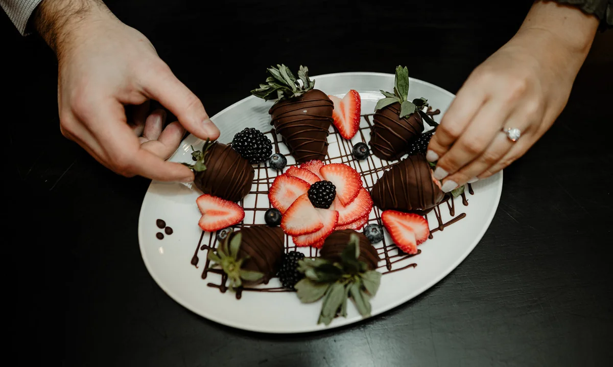 two hands placing strawberries on a plate of chocolate covered strawberries with blackberries at the Wentworth inn.