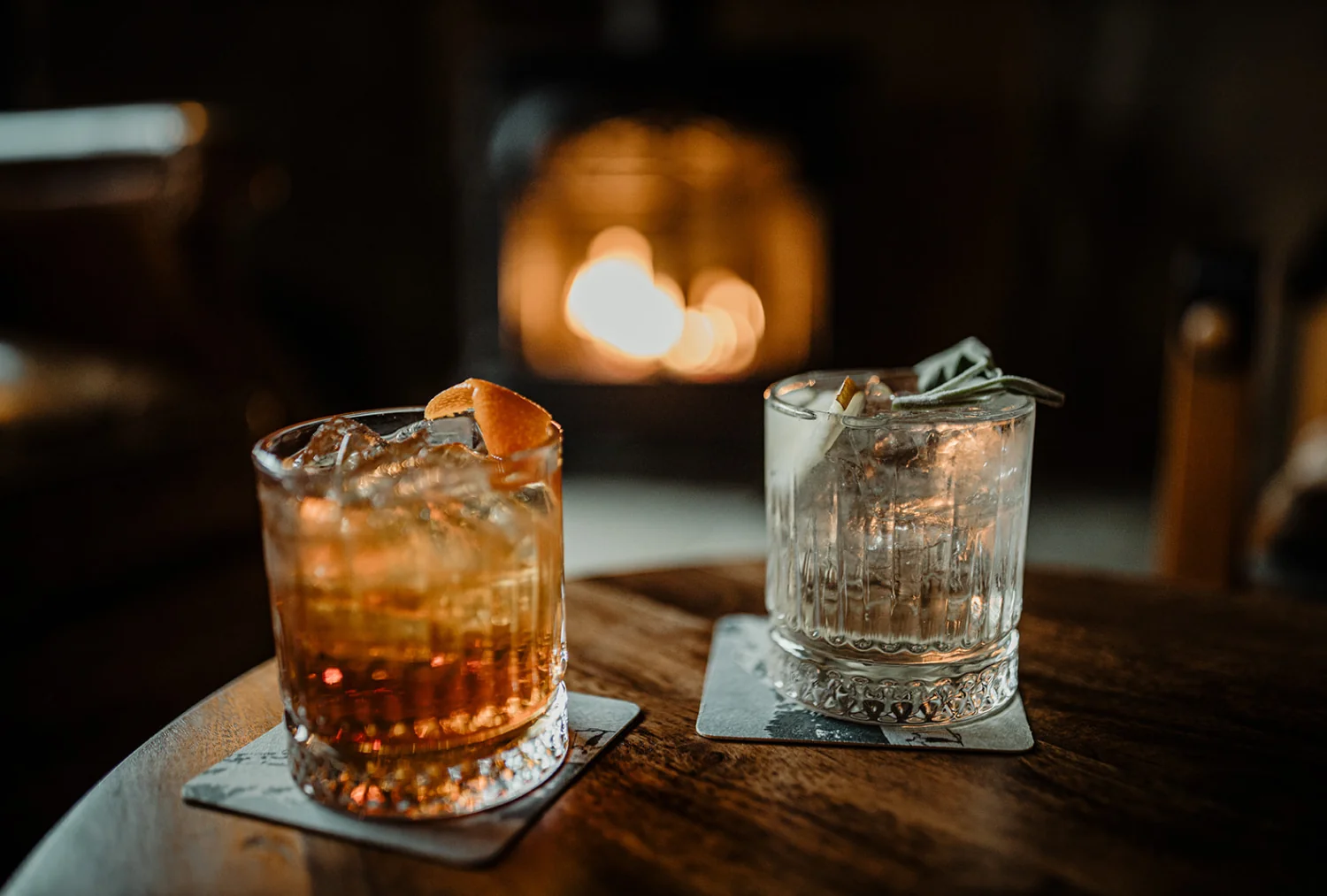 Two glasses with ice on a table in front of a burning woodstove
